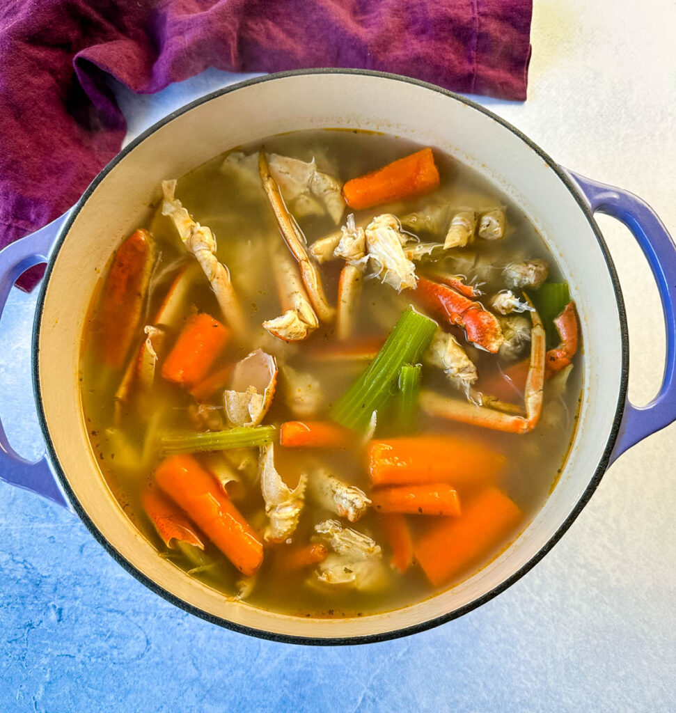 homemade seafood stock with crab shells, carrots, and celery in a Dutch oven