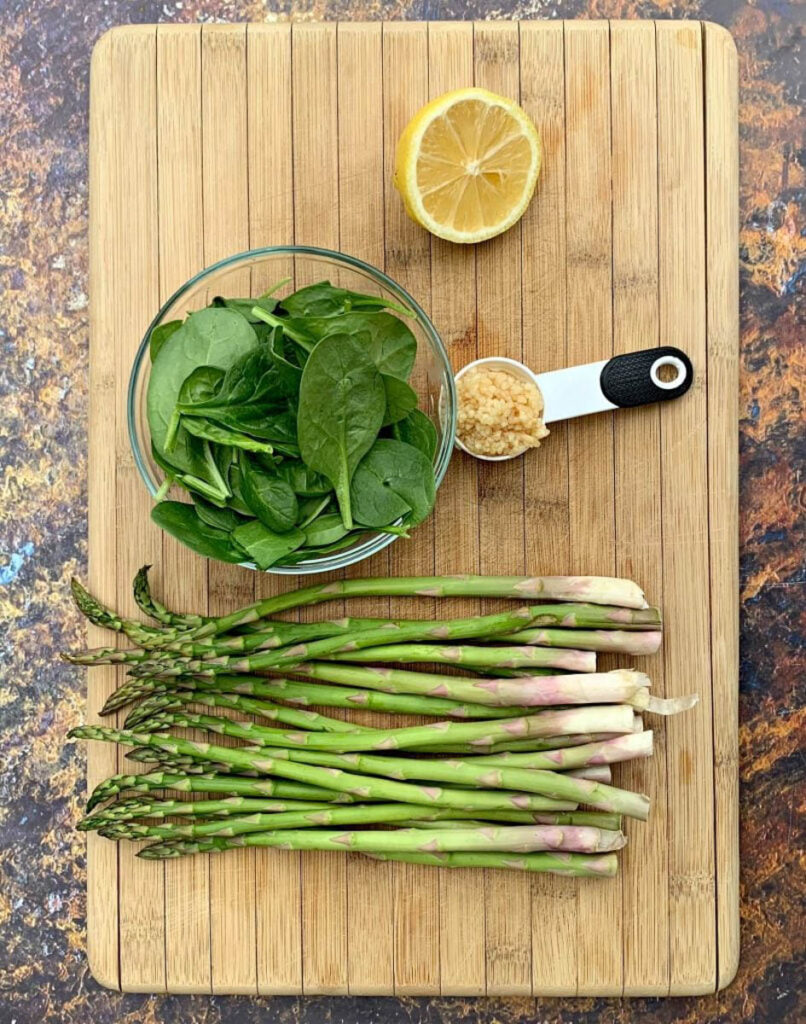 fresh asparagus, fresh lemon, garlic, and fresh spinach in separate bowls