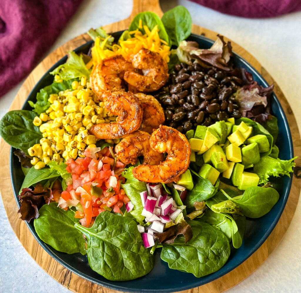 shrimp taco salad with avocado, corn, black beans, onions and salsa on a blue plate
