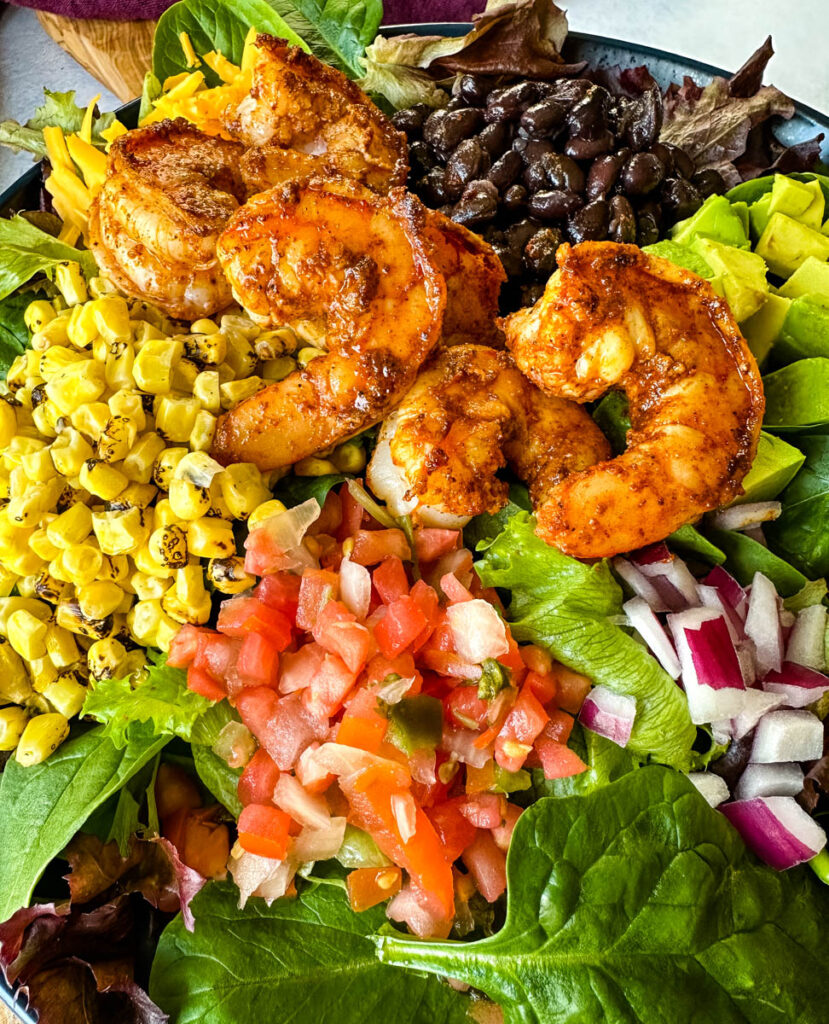 shrimp taco salad with avocado, corn, black beans, onions and salsa on a blue plate
