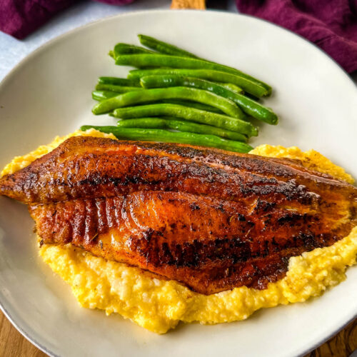 blackened fish on a plate with grits and green beans