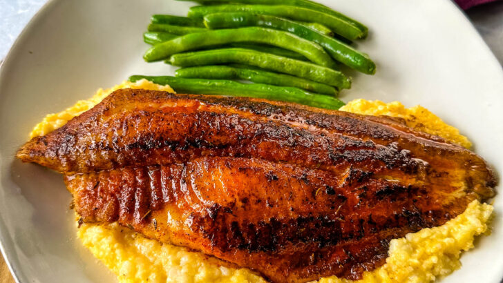 blackened fish on a plate with grits and green beans