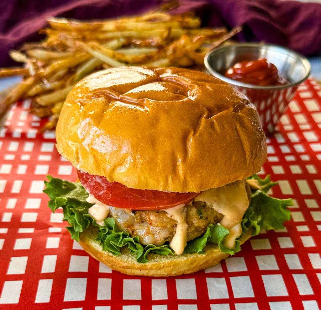 shrimp burger on a brioche bun with lettuce, tomatoes, and spicy mayo
