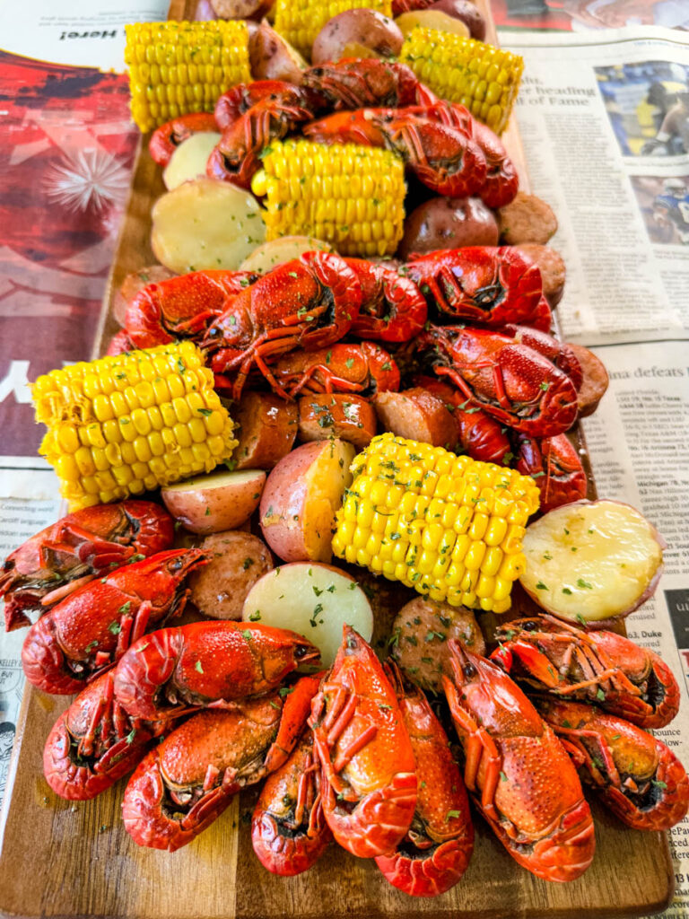 crawfish boil on a platter with corn, red potatoes, sausage, and butter with newspaper