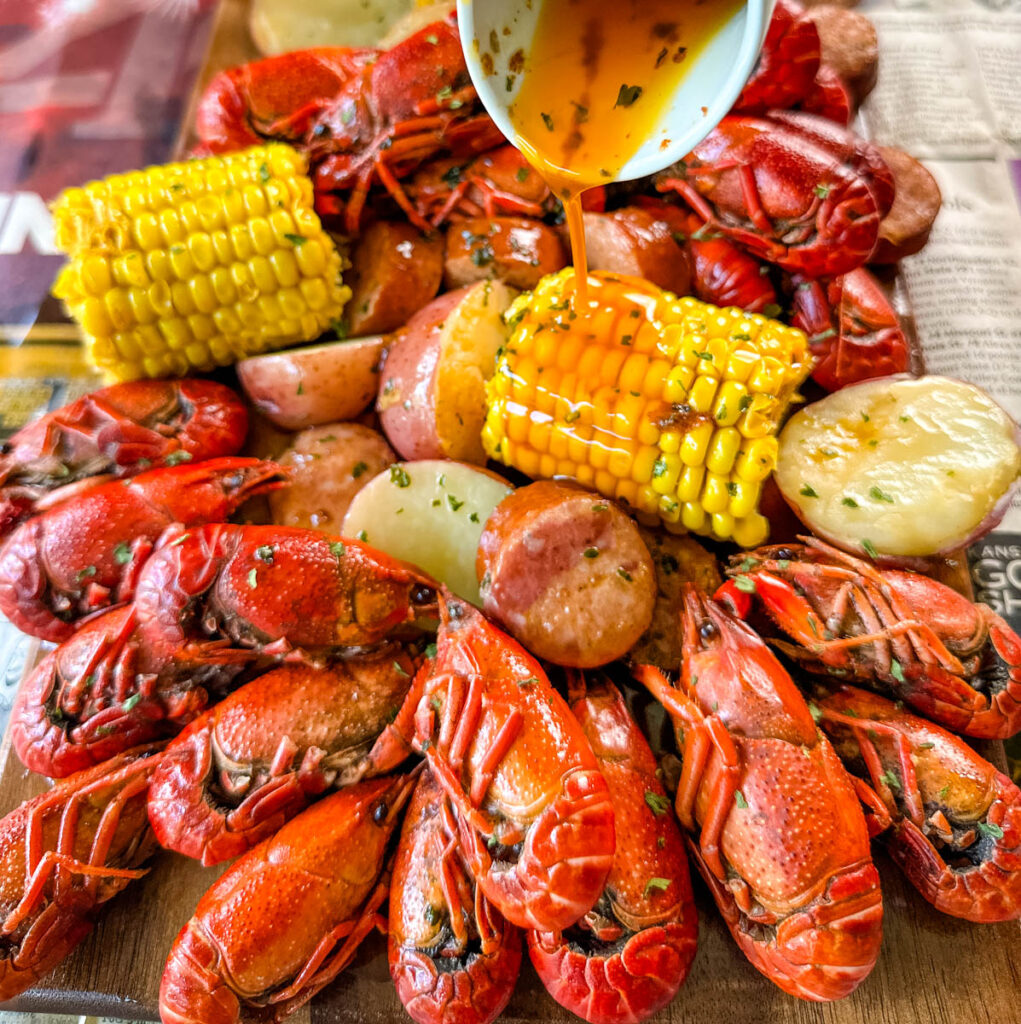 crawfish boil on a platter with corn, red potatoes, sausage, and butter with newspaper