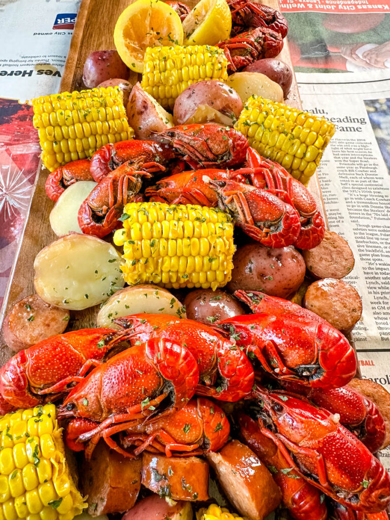 crawfish boil on a platter with corn, red potatoes, sausage, and butter with newspaper