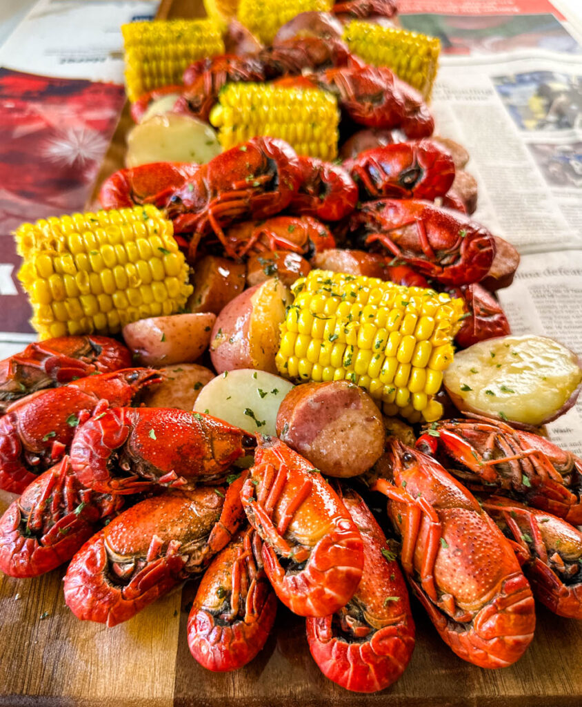 crawfish boil on a platter with corn, red potatoes, sausage, and butter with newspaper