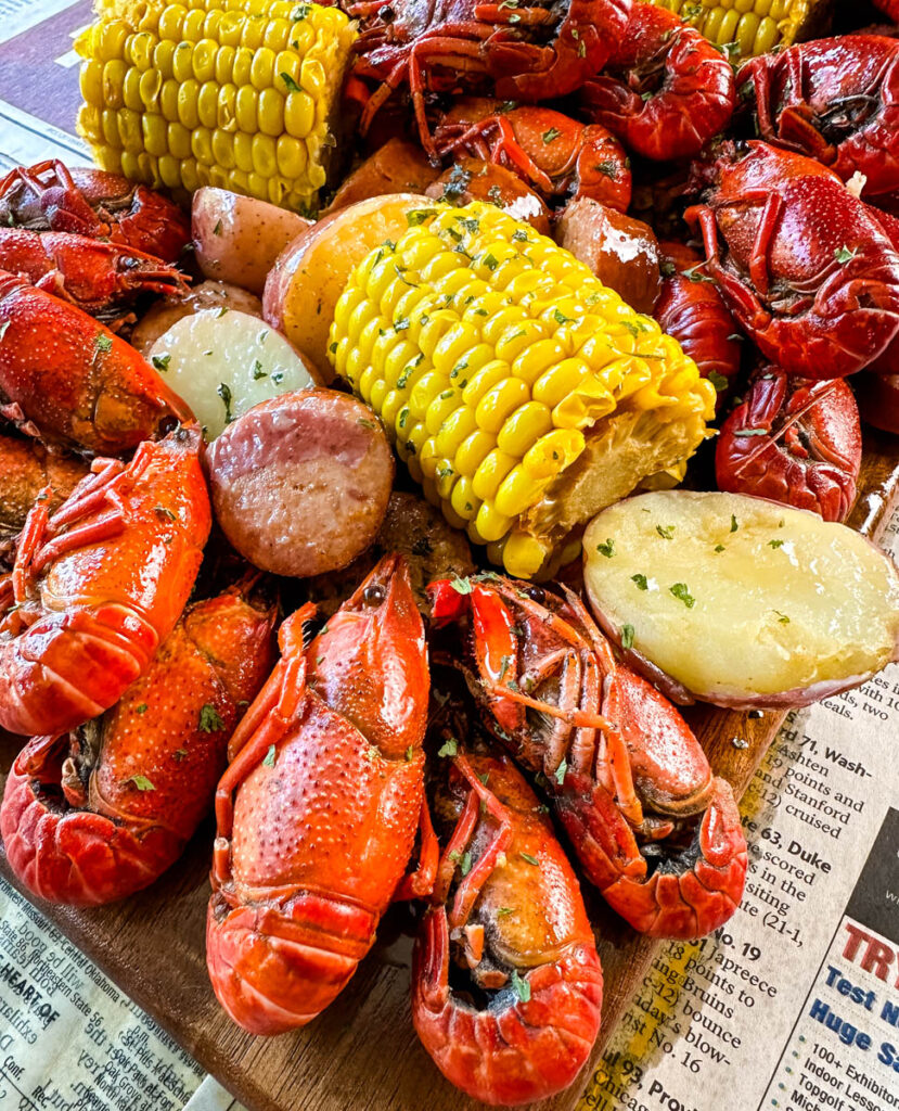 crawfish boil on a platter with corn, red potatoes, sausage, and butter with newspaper