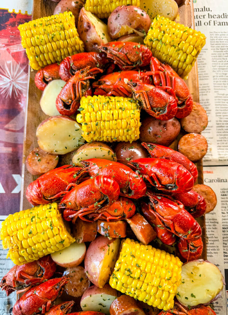 crawfish boil on a platter with corn, red potatoes, sausage, and butter with newspaper