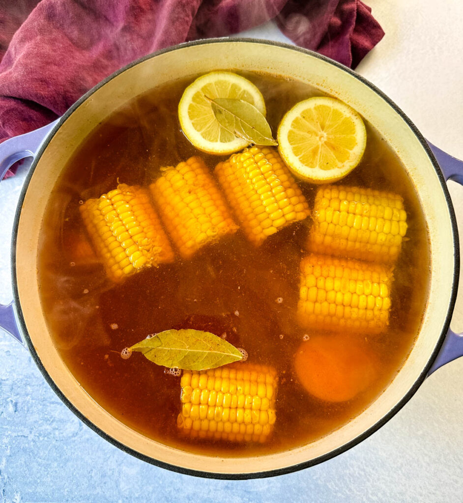 corn on the cob, lemon, bay leaf, potatoes, and sausage in a large Dutch oven with crawfish boil sauce