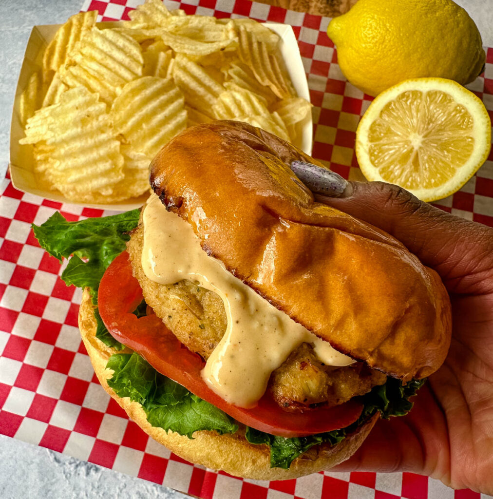 person holding crab cake sandwich with chips