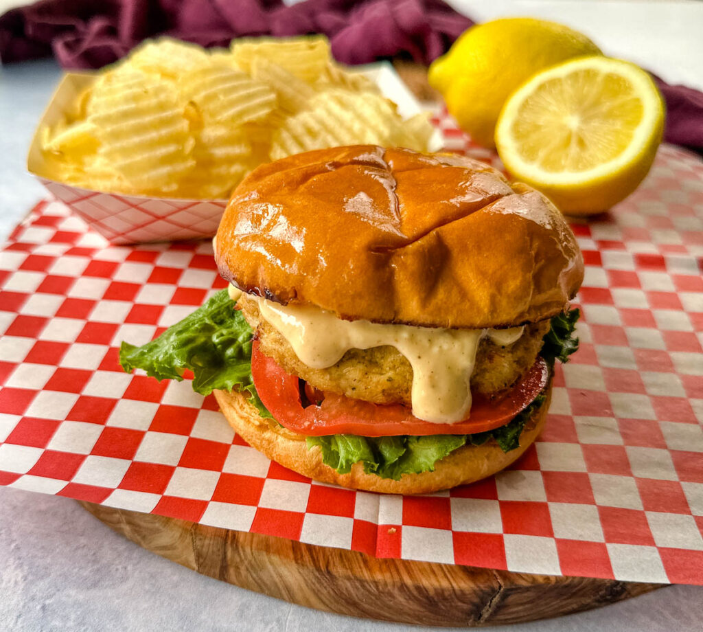 crab cake sandwich on a brioche bun with lettuce tomatoes and a side of chips with remoulade sauce