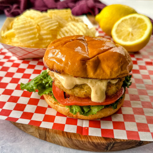 crab cake sandwich on a brioche bun with lettuce tomatoes and a side of chips with remoulade sauce
