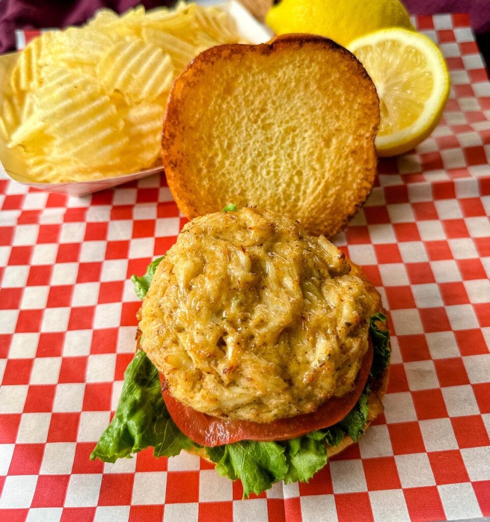 crab cake sandwich on a brioche bun with lettuce tomatoes and a side of chips