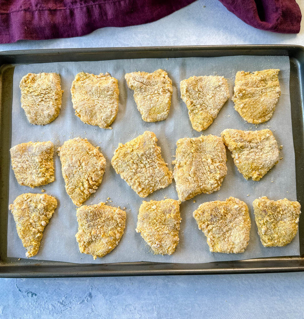 breaded catfish nuggets on a sheet pan with parchment paper