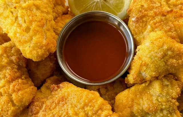 breaded catfish nuggets on a plate with hot sauce and a fresh lemon