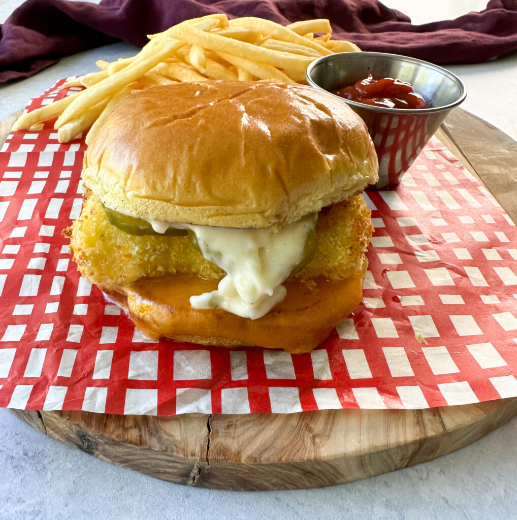 fish sandwich with cheese, pickles, and tartar sauce on a brioche bun on a plate with fries