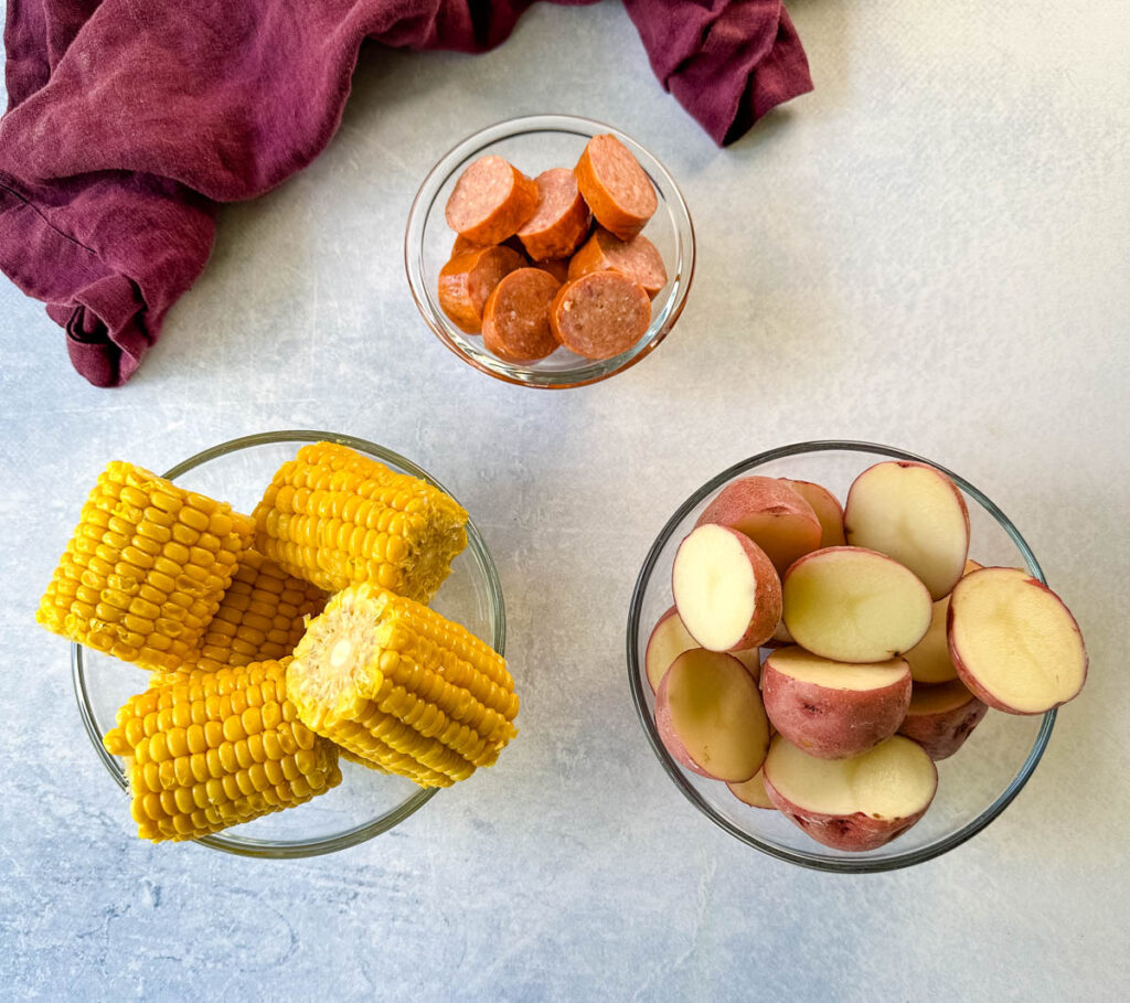 andouille sausage, corn on the cob, and red potatoes in separate glass bowls
