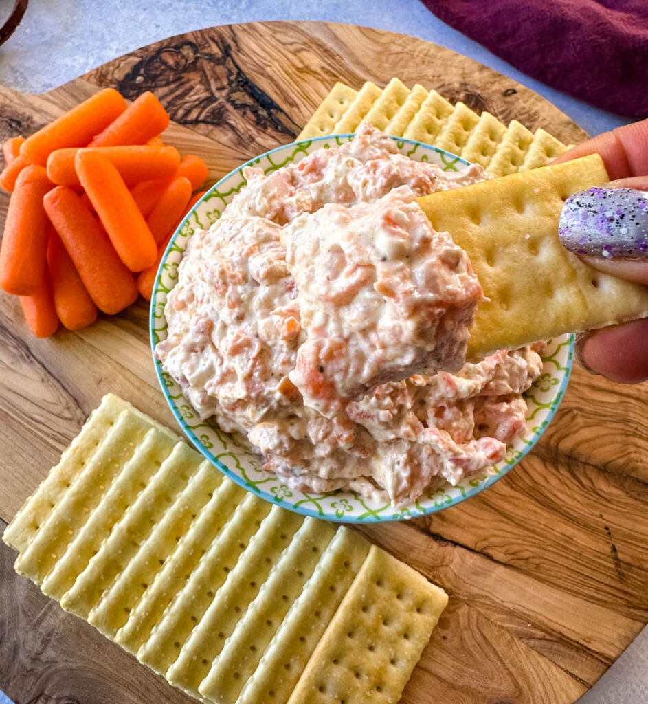 person holding a cracker filled with smoked fish dip with salmon