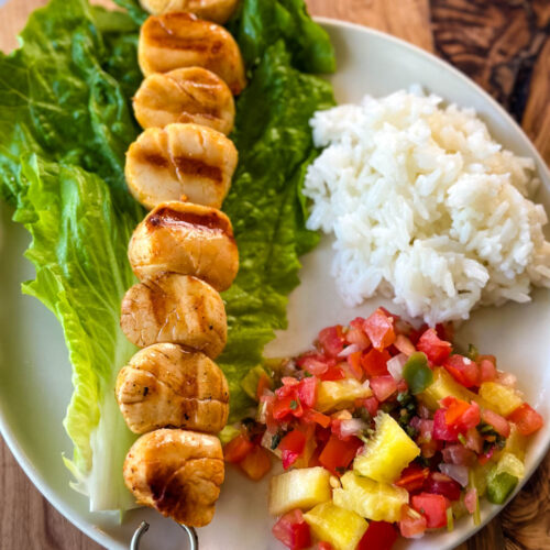 grilled scallops on a plate with lettuce, rice, and vegetables