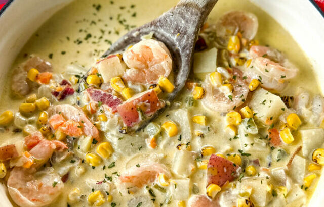 shrimp and corn chowder with bacon and potatoes with a wooden spoon in a Dutch oven