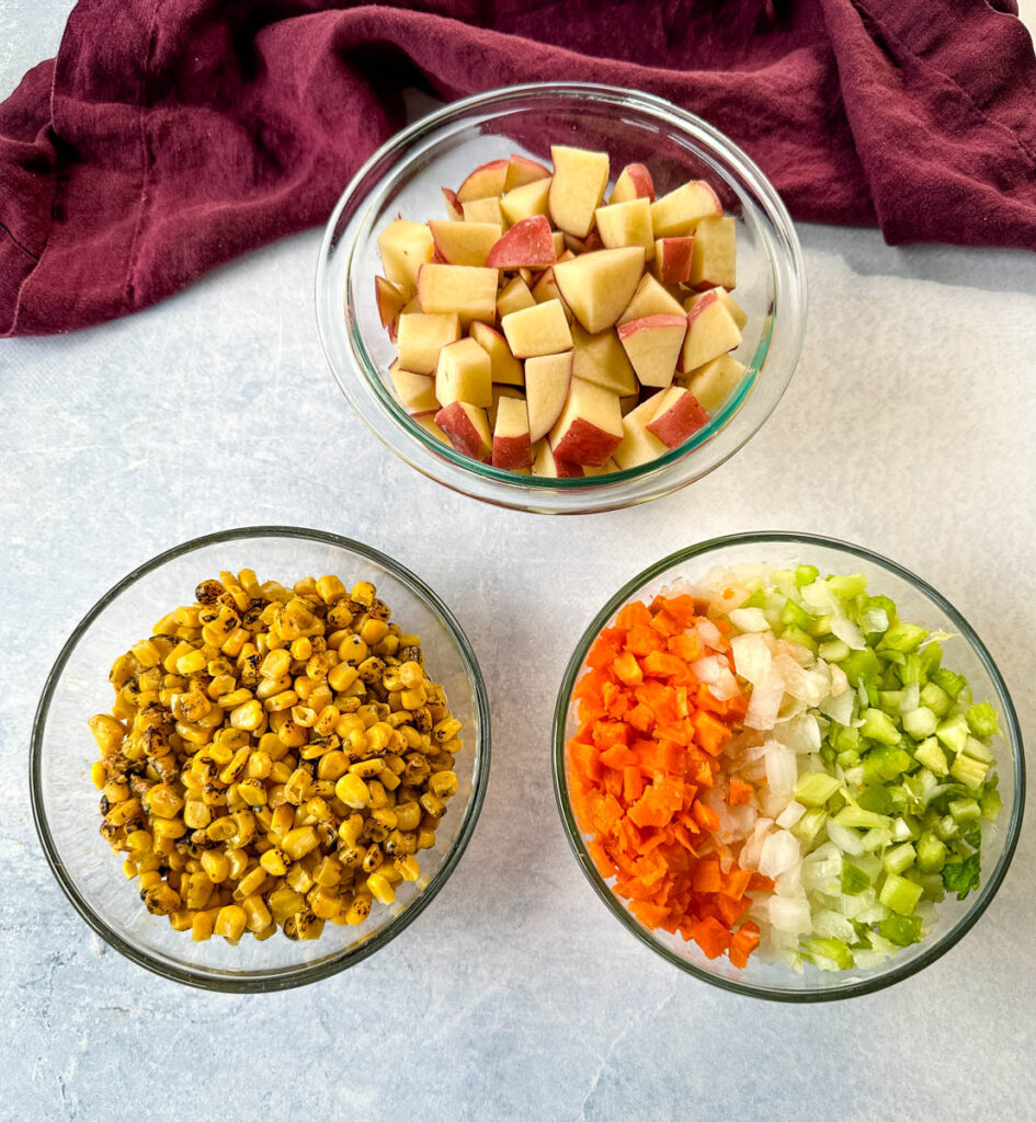 raw red potatoes, corn, carrots, celery, and onions in separate glass bowls
