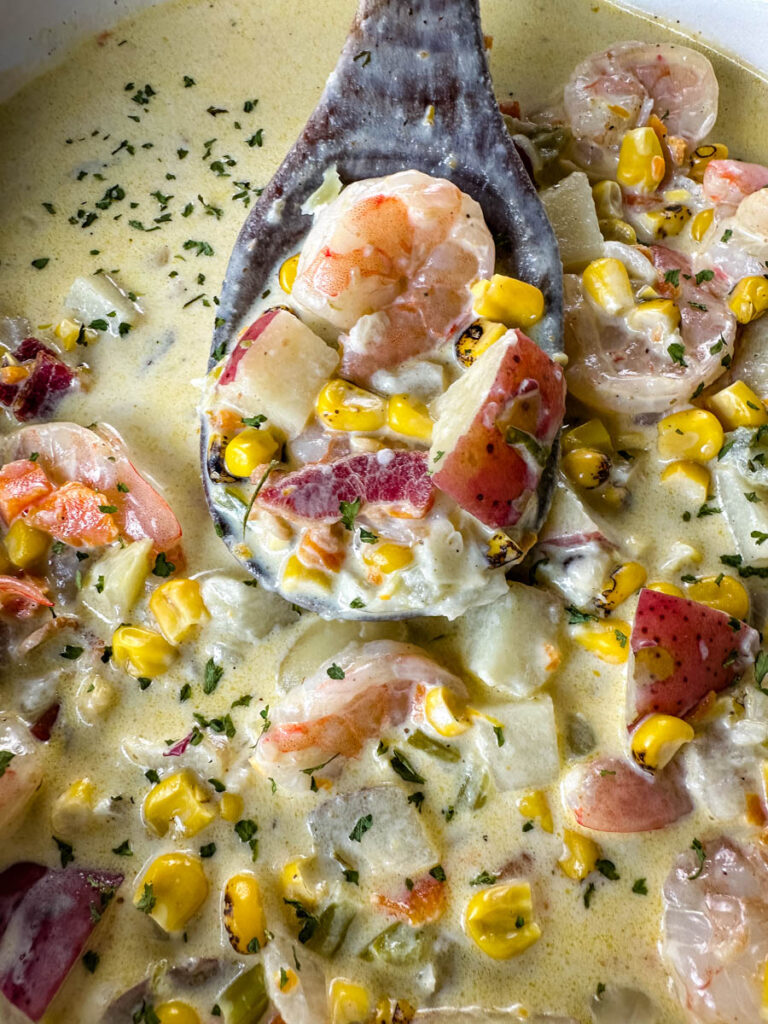 shrimp and corn chowder with bacon and potatoes with a wooden spoon in a Dutch oven