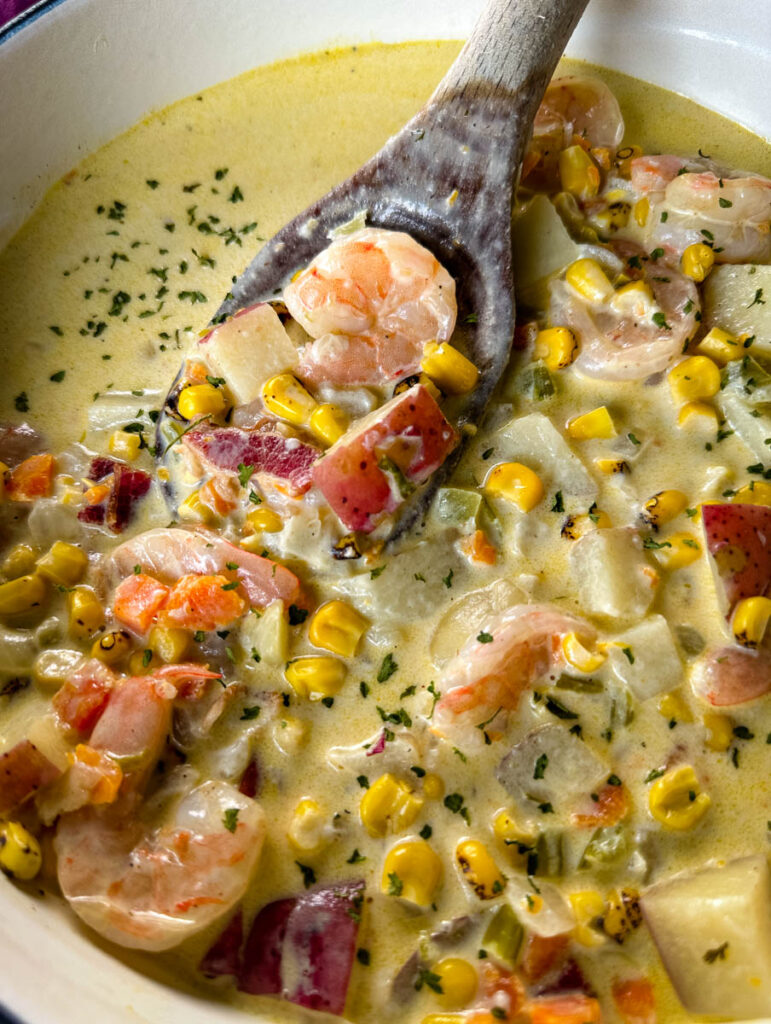shrimp and corn chowder with bacon and potatoes with a wooden spoon in a Dutch oven