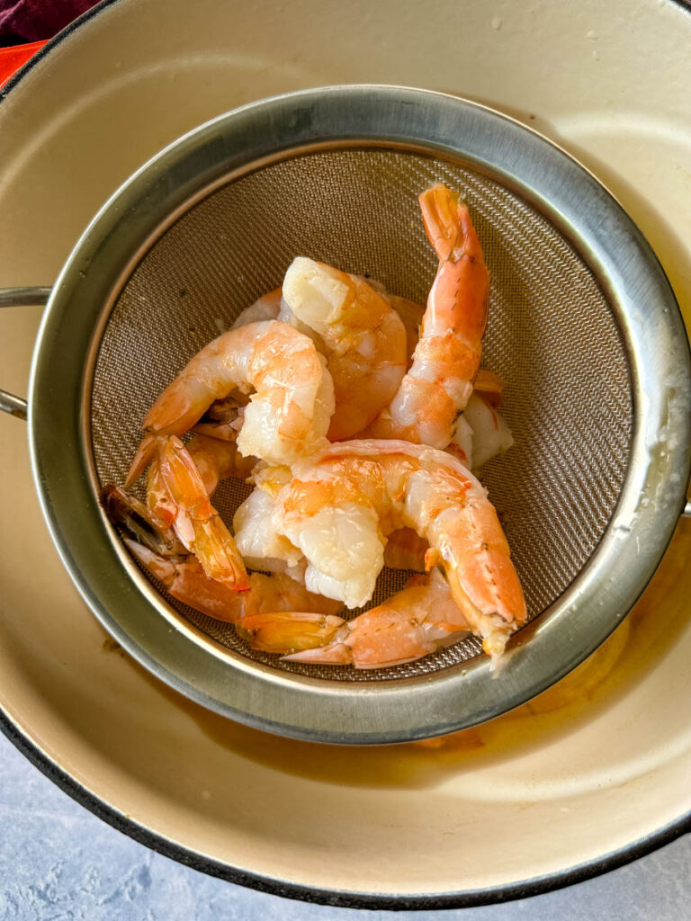 raw shrimp in a strainer inside a pot with hot water