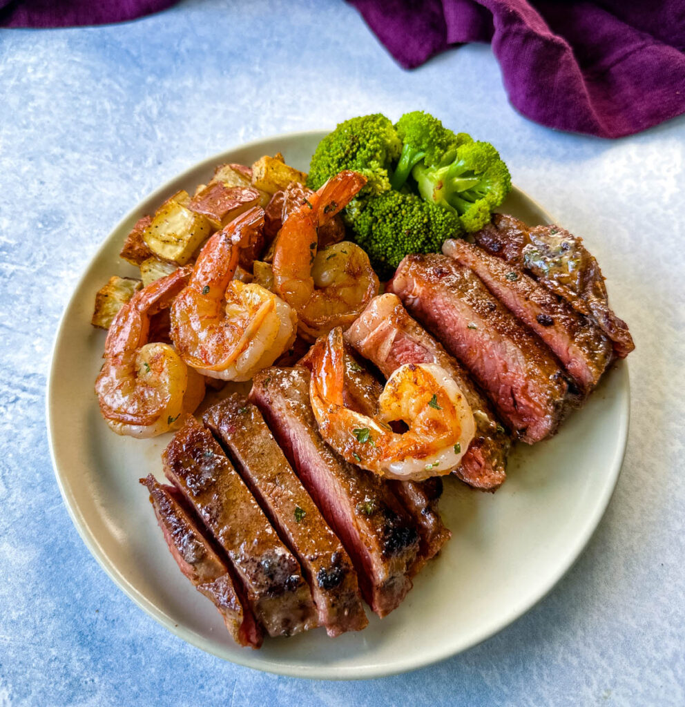 sliced steak and shrimp on a plate with cooked potatoes and broccoli