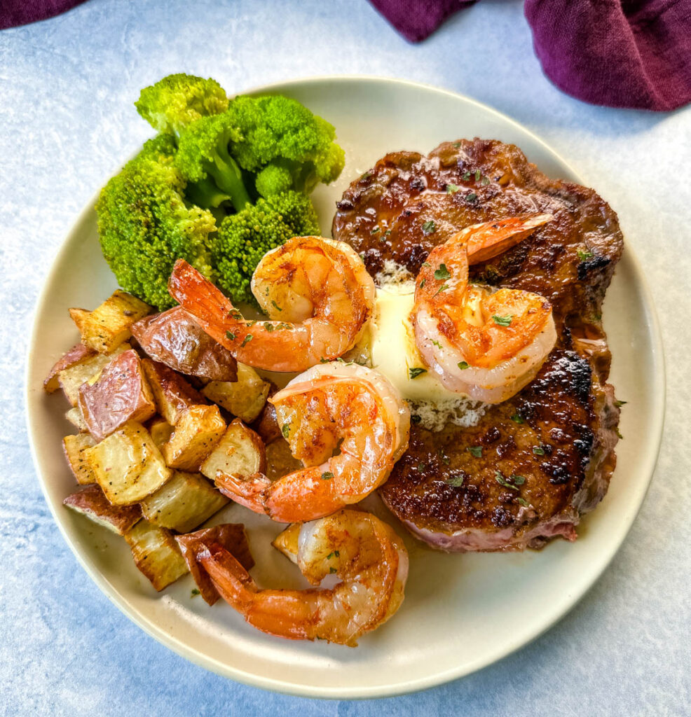 steak and shrimp on a plate with cooked potatoes and broccoli