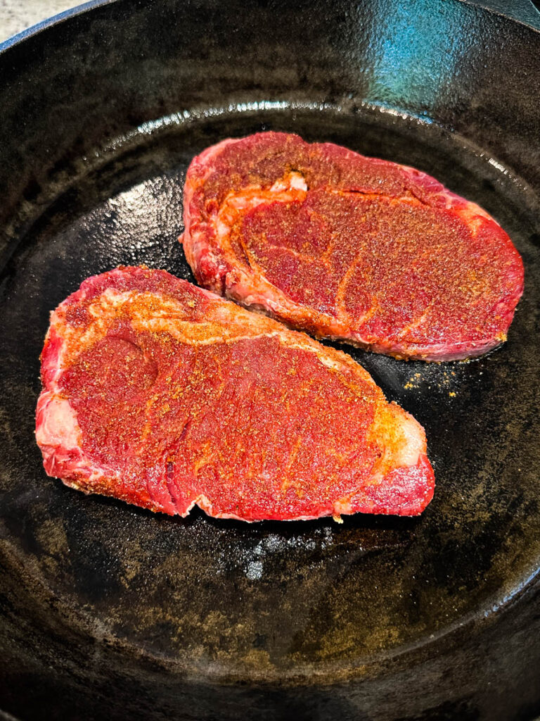 raw seasoned steaks in a cast iron skillet