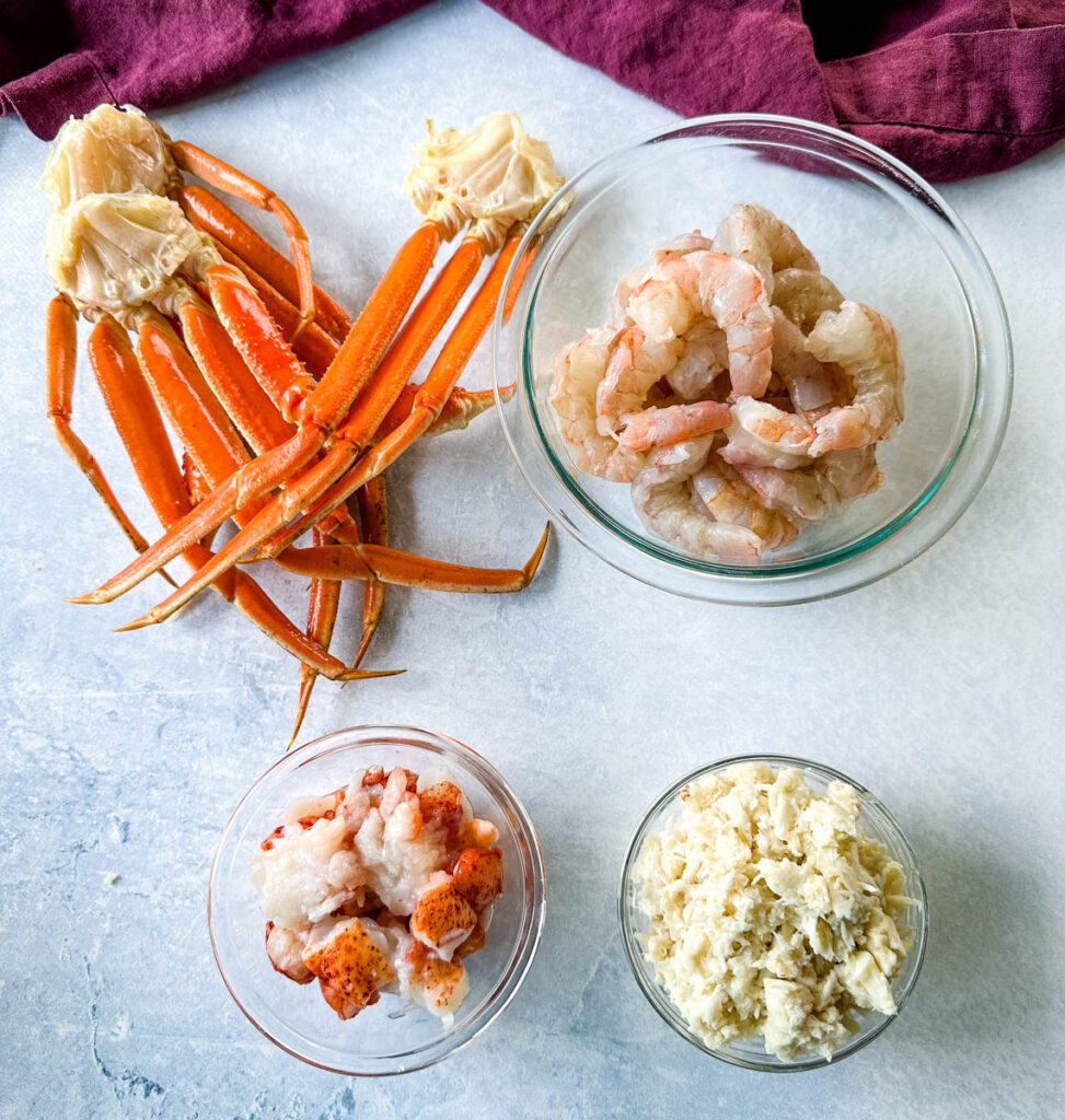 snow crab legs, raw shrimp, lobster, and lump crab meat in separate glass bowls