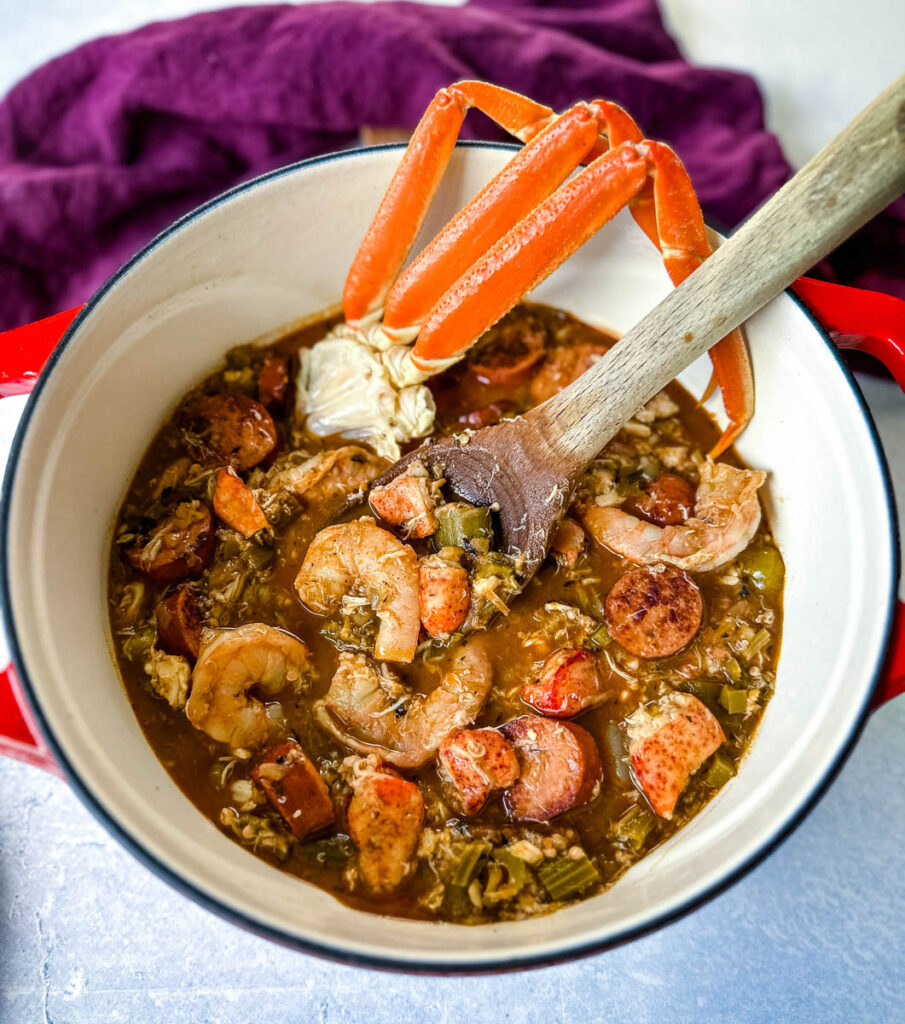 Cajun seafood gumbo with shrimp and crab meat and crab legs with rice in a Dutch oven with a wooden spoon
