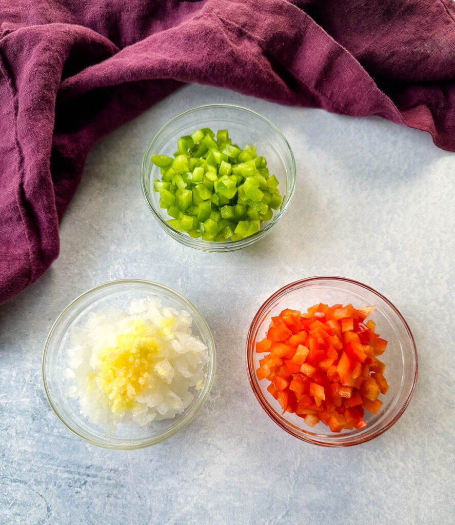 chopped green peppers, red peppers, onions, and garlic in separate glass bowls