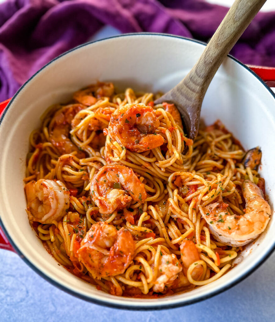 shrimp spaghetti with garlic in a Dutch oven with a wooden spoon