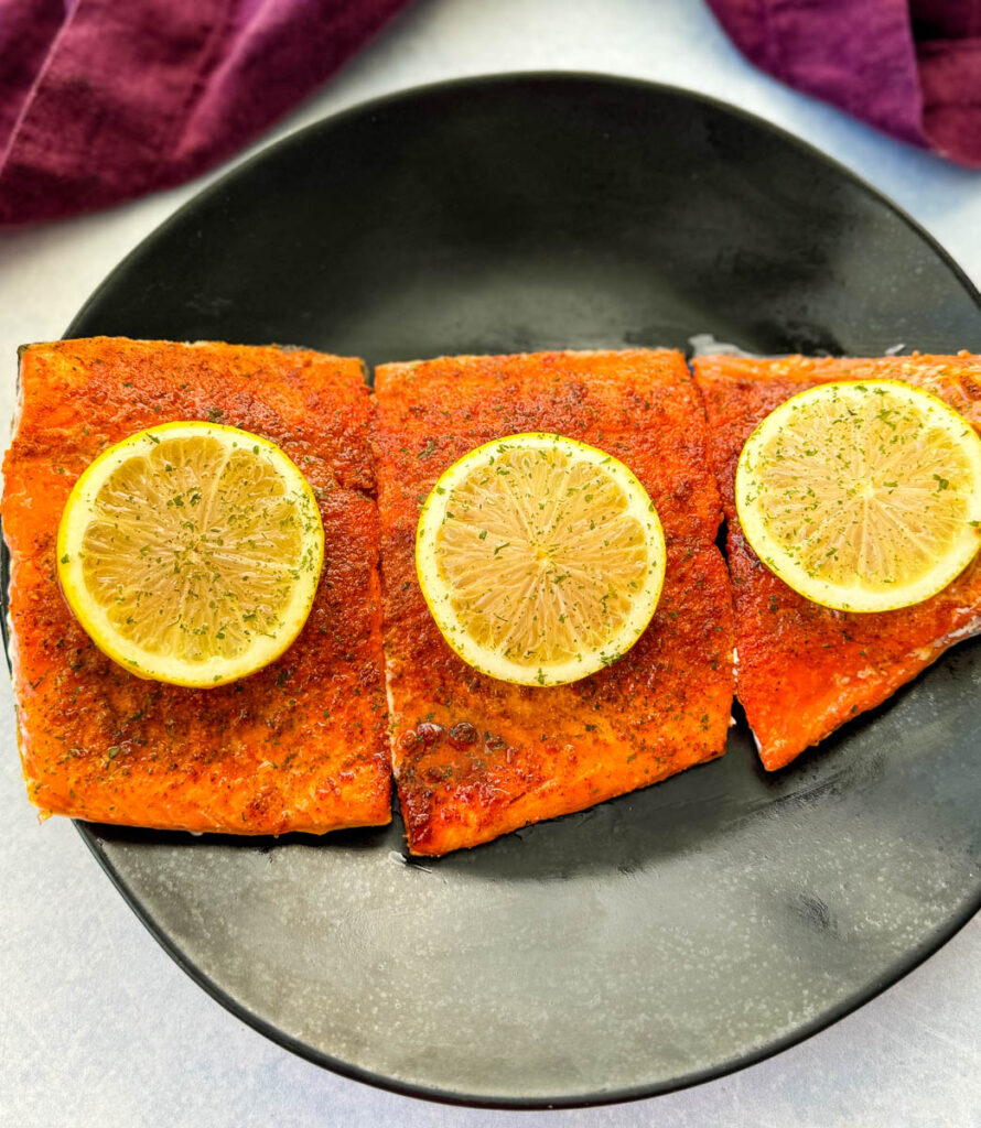baked salmon fillets on a black plate with fresh lemons