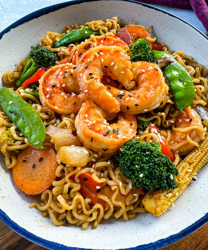 shrimp stir fry with noodles, vegetables, and a homemade sauce in a white bowl
