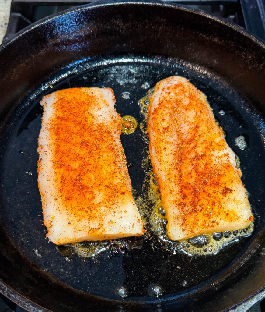 seasoned cod fish fillets in a cast iron skillet with butter