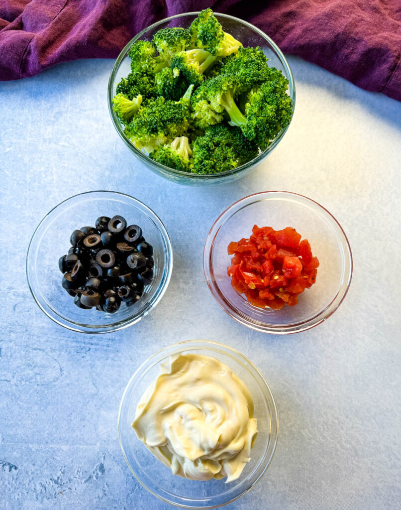broccoli, olives, tomatoes, and mayo in separate glass bowls